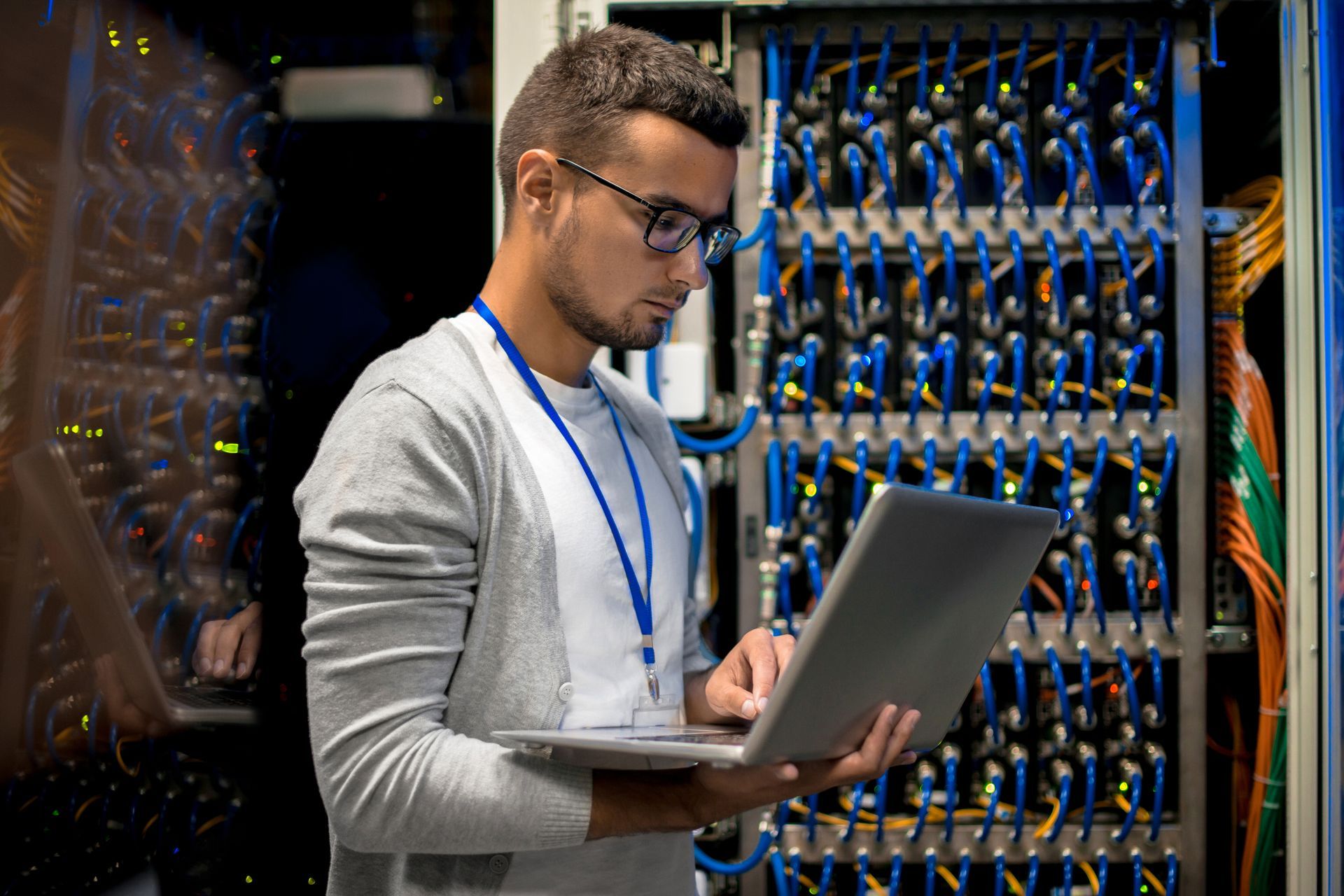 a man wearing glasses is using a laptop in a server room