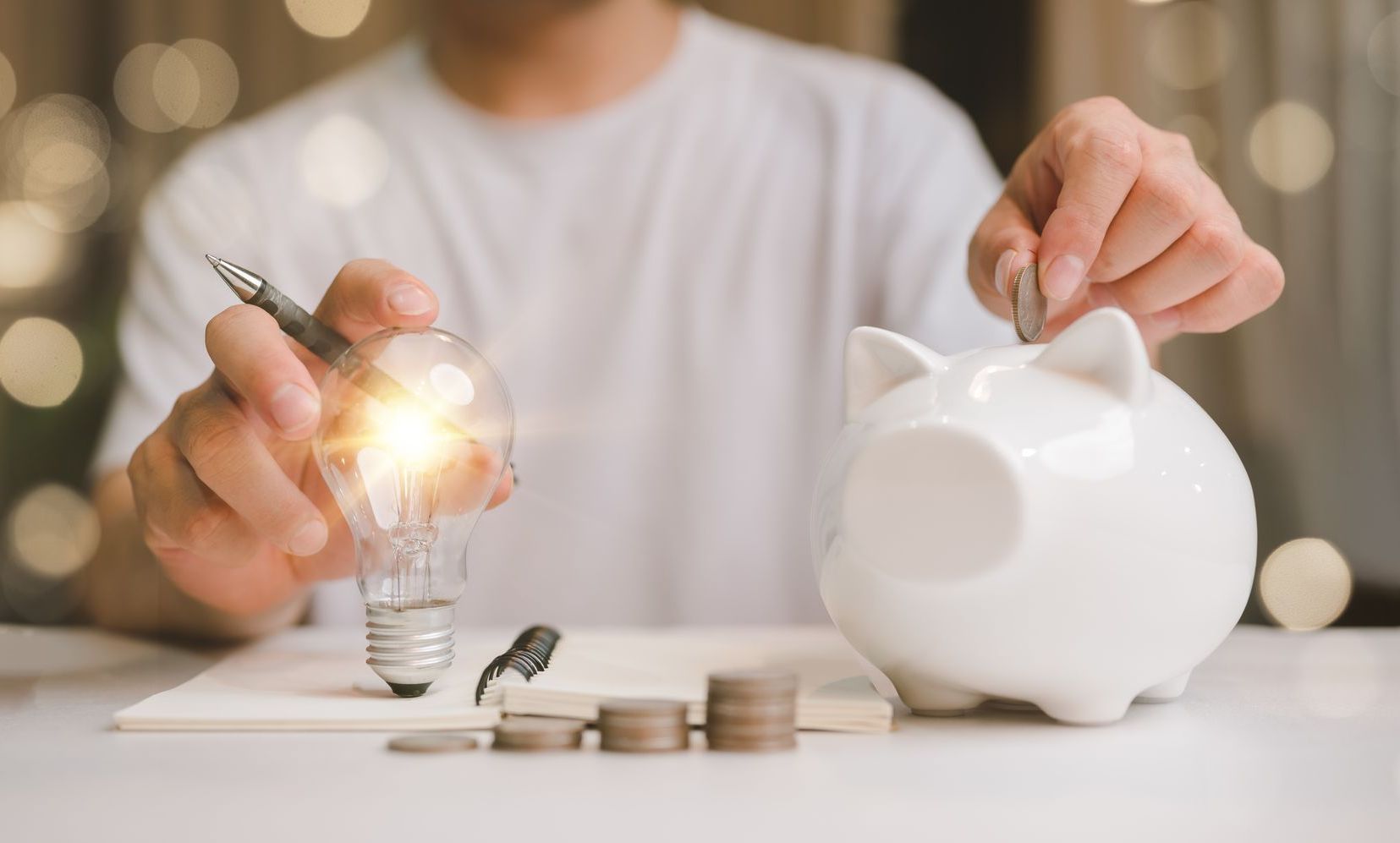 A man is putting a light bulb into a piggy bank.