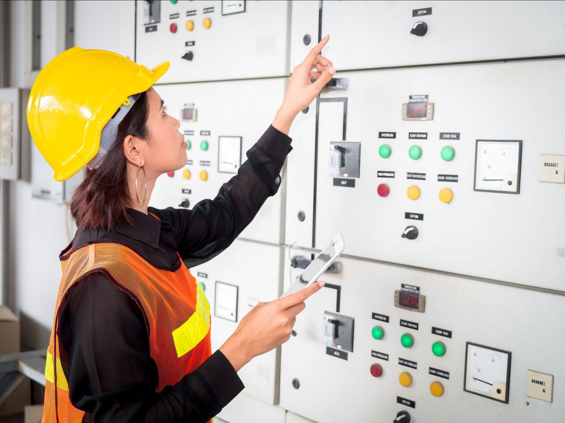 a woman wearing a hard hat is pointing at a control panel