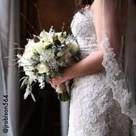 Bride in a lace wedding dress holding a white bouquet beside a curtain