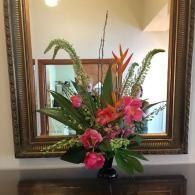 Floral arrangement with pink and orange flowers in a vase on a table, reflected in a framed mirror