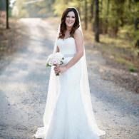 Bride in a white gown holding a bouquet on a tree-lined path