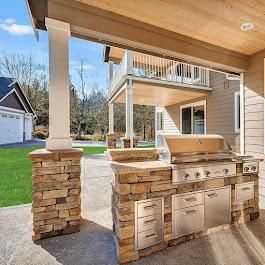 Outdoor kitchen with stone accents, stainless steel grill, and cabinetry under a covered patio.
