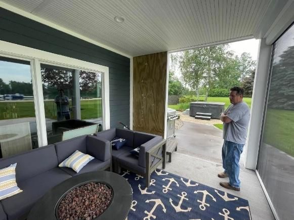 Man stands on a screened porch looking toward a backyard with a hot tub.
