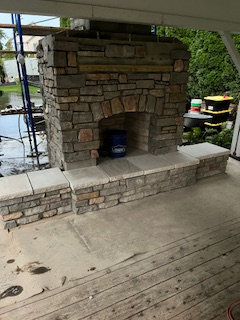 Stone fireplace and hearth under construction on a wooden porch.