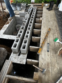 Construction of a deck; cinder blocks and lumber are being used. A person is standing nearby.