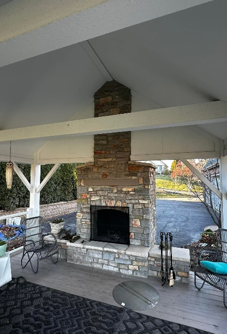 Stone fireplace on a covered patio, with seating and a dark rug.