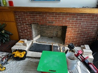 Fireplace under construction, tools and materials scattered. Brick and stone, interior setting.
