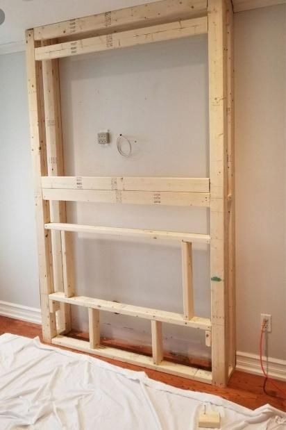 Wooden frame for built-in shelving and media niche, constructed against a white wall.