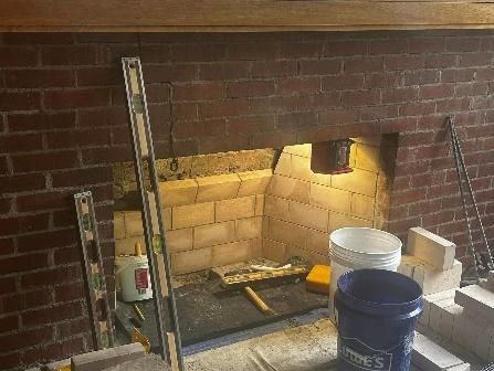 Fireplace under construction, brick and firebrick interior, tools and buckets present.