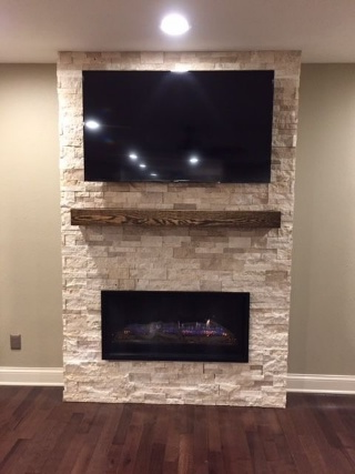Stone fireplace with mounted TV and wooden mantel. Dark hardwood floor and beige walls.