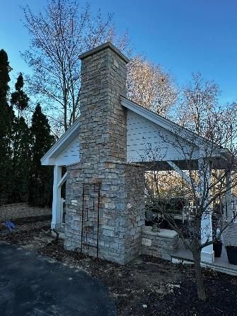 Stone chimney on a white-roofed structure with a blue sky background and bare trees.