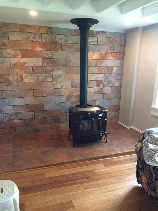 Wood-burning stove centered against a stone accent wall, on tile flooring, with wood flooring in foreground.