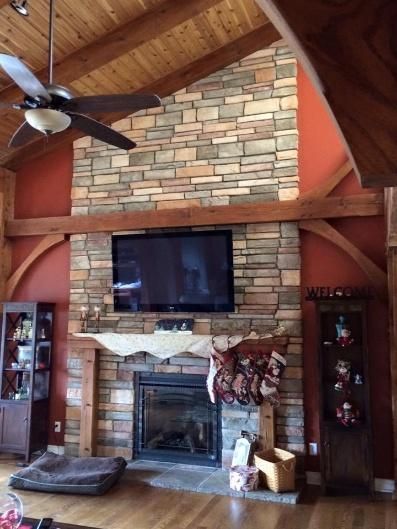 Fireplace with stone surround, TV, wood beams, and vaulted ceiling in a rustic living room.