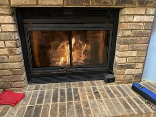 Fireplace with burning fire, enclosed by glass doors in a brick surround.
