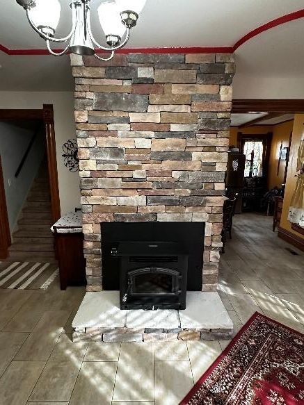 Stone-faced fireplace with black insert, set in a home. The floor is light, and a rug lies to the right.