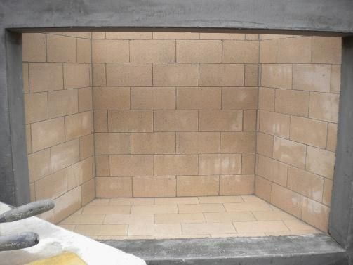 Fireplace interior with light-colored brick walls and floor, framed by a dark gray opening.