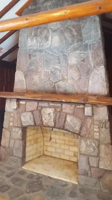 Stone fireplace with arched opening and wooden mantel, set in a wood-paneled room.