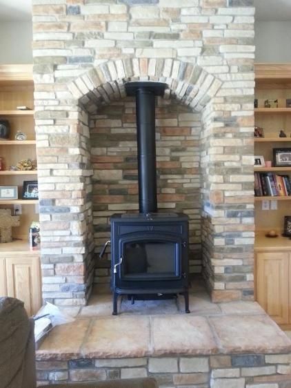 Stone fireplace with wood-burning stove inside an arched alcove. Built-in bookshelves on either side.