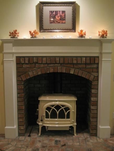 Fireplace with arched brick interior, white mantle, and cream-colored wood-burning stove. Artwork and orange decorations.