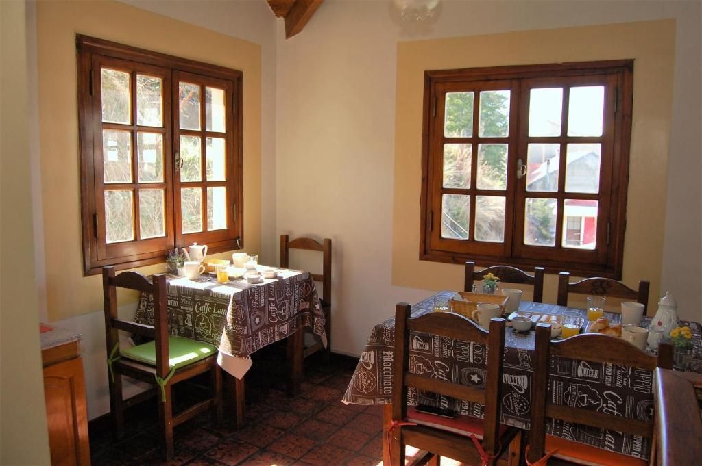 Acogedor comedor con mesas y sillas de madera junto a ventanas soleadas, vajilla puesta para una comida.