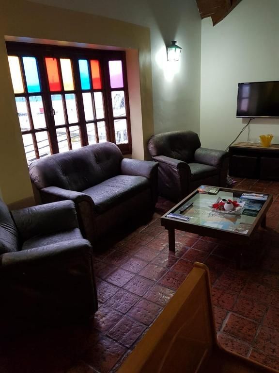 Acogedora sala de estar con sofás oscuros, mesa de centro, vidriera, aplique de pared y televisor montado en la pared.