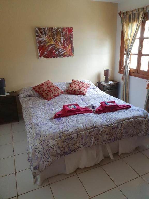 Habitación con cama de matrimonio, almohadas rojas, mesitas de noche y luz natural que entra por la ventana.