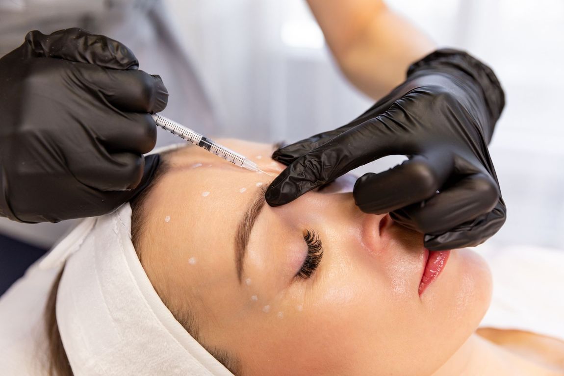 Cosmetic injection being administered to a woman’s forehead while lying on a treatment bed