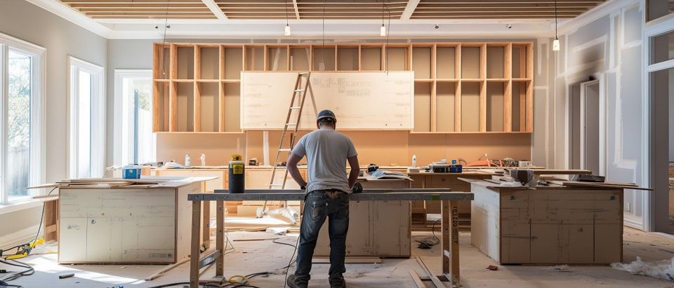 Construction worker in a kitchen under renovation. Cabinets and tools are visible.
