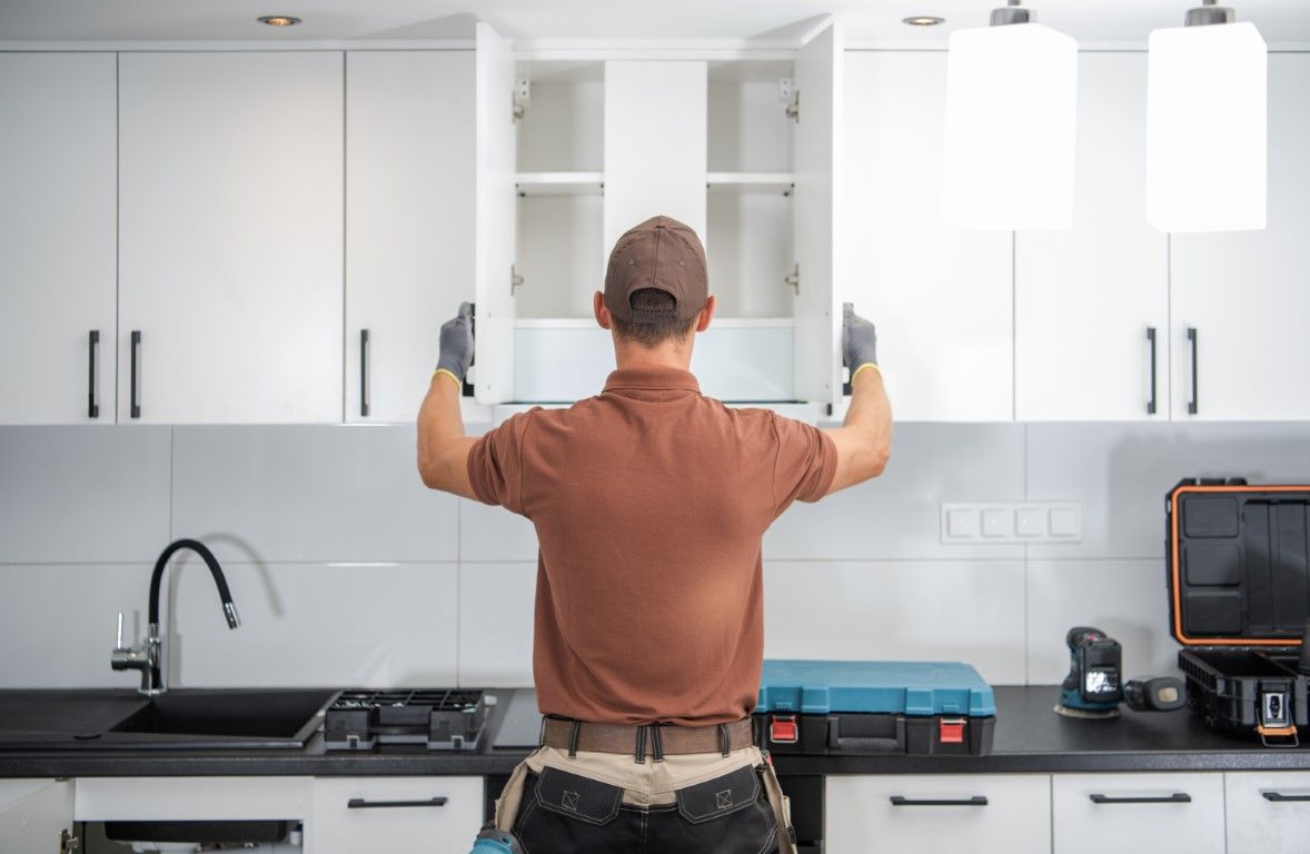Person in a brown shirt installing a white kitchen cabinet, with tools visible on the counter.
