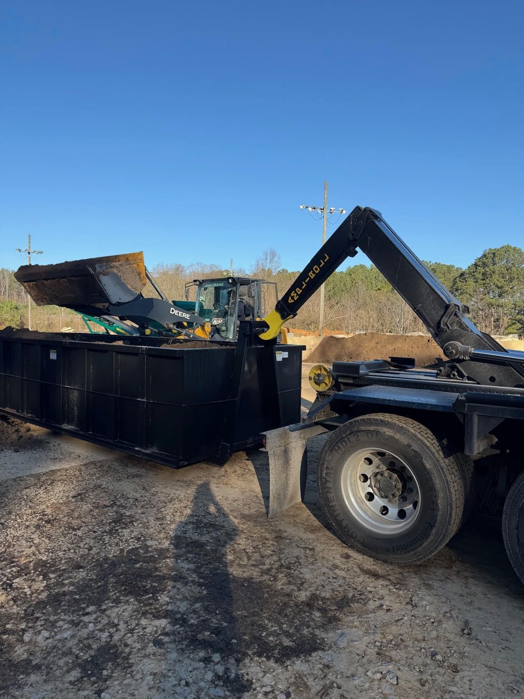 A dumpster is being loaded with dirt by a dump truck.