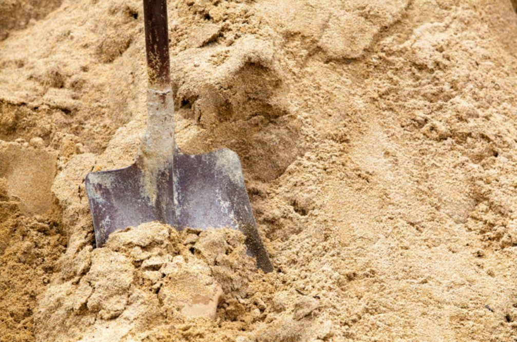 A shovel is sticking out of a pile of masonry sand.