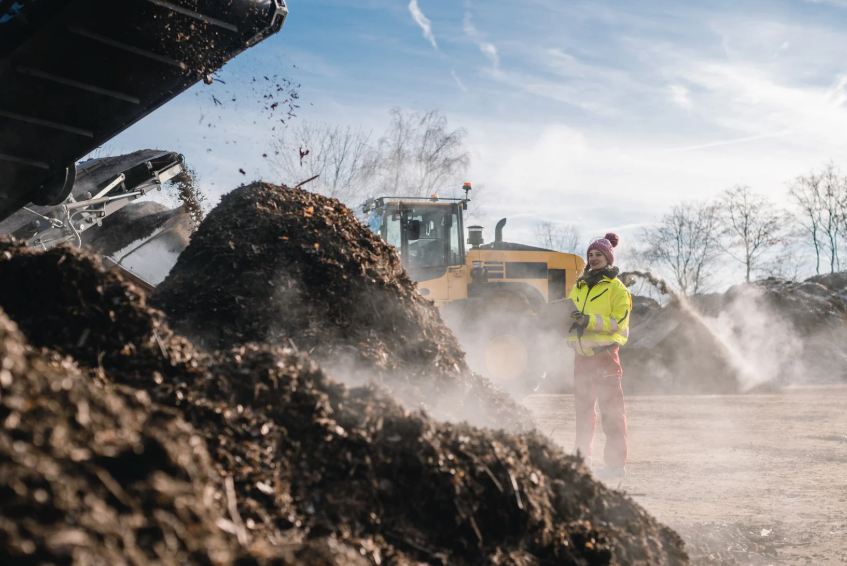 A man is standing in front of a pile of dirt with a bulldozer in the background.