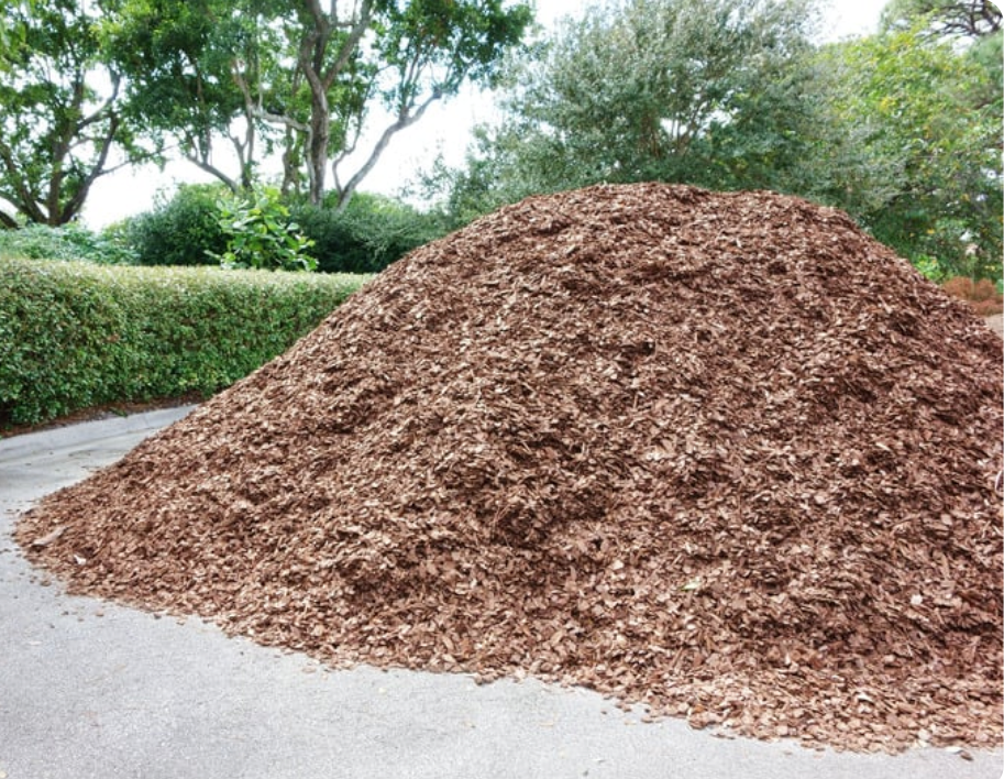 A large pile of wood chips sits on the side of a driveway