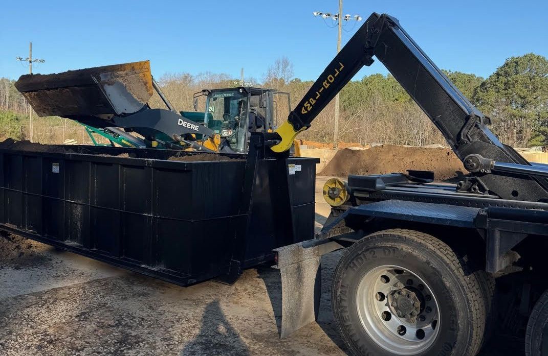 A dumpster is being loaded with dirt by a tractor.