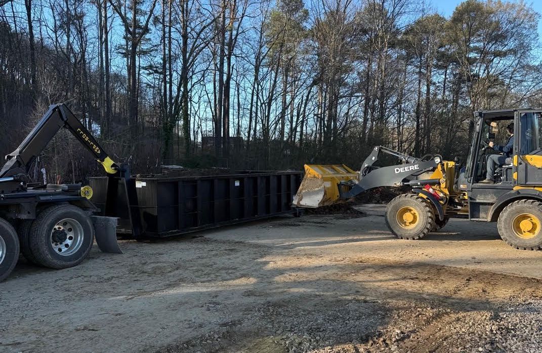 A dump truck and a front end loader are parked in a dirt lot.
