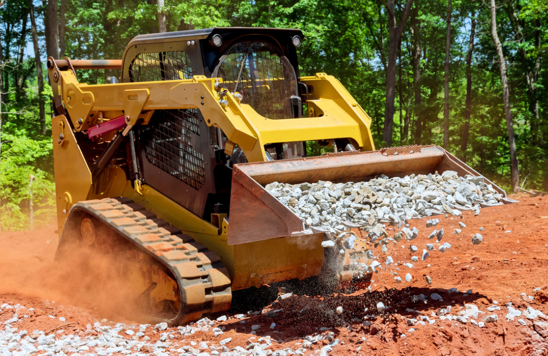 A skidsteer is moving gravel and rocks on a construction site.
