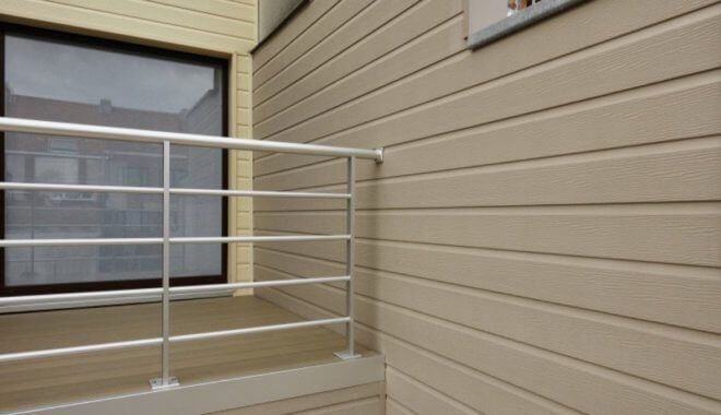 Buitenaanzicht van een gebouw met beige gevelbekleding, zilveren leuning, raam en deur.