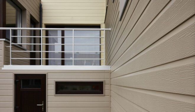 Beige gevelbekleding op modern gebouw met witte leuning en donkere deur.