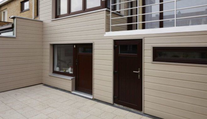 Beige gevelbekleding en terras omringen een bruine deur en ramen.
