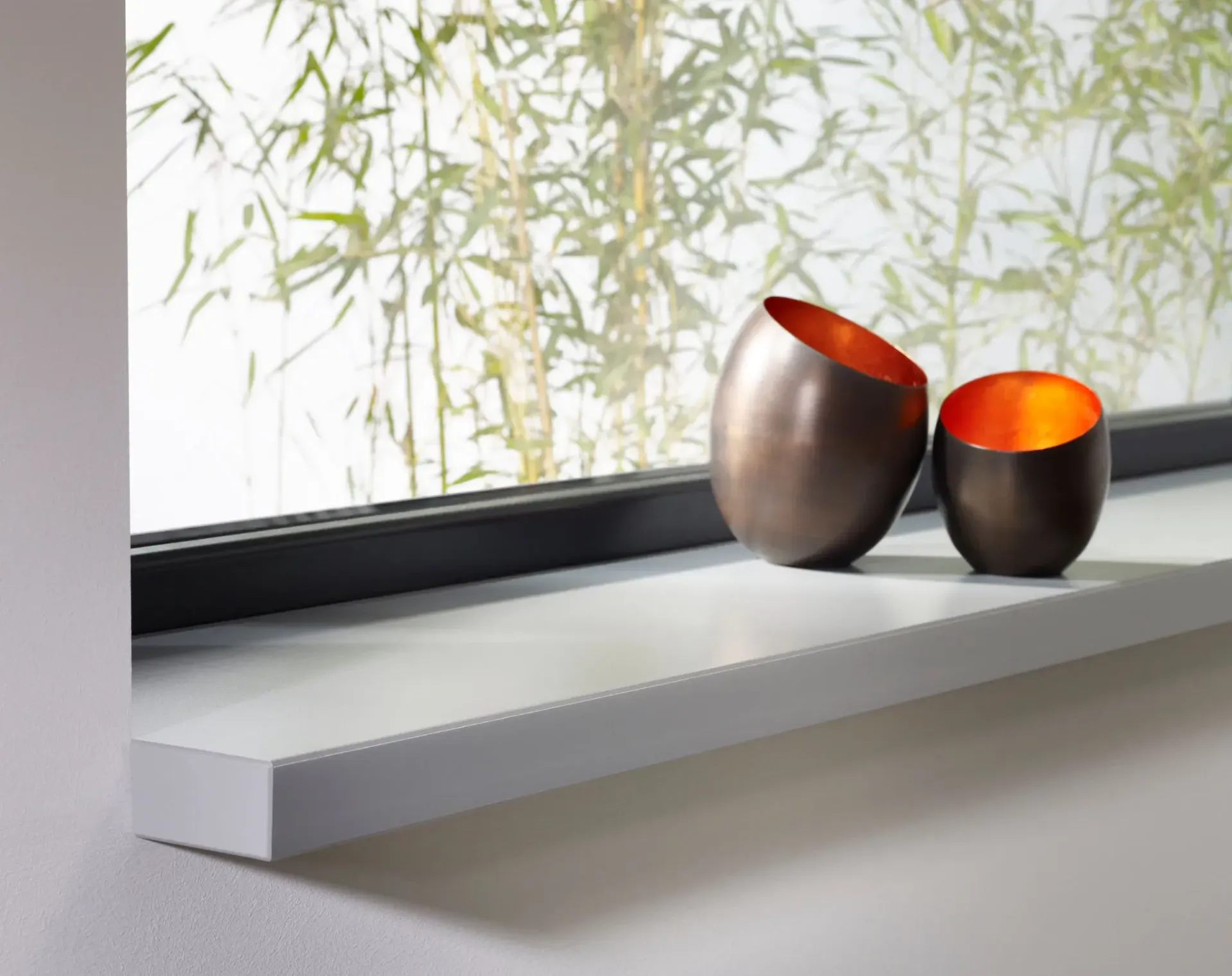 Twee bronzen kaarsenhouders op een witte vensterbank, met bamboe op de achtergrond.