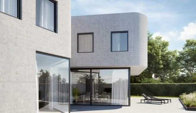 Modern betonnen huis met grote glazen ramen en terras, zonnige dag.