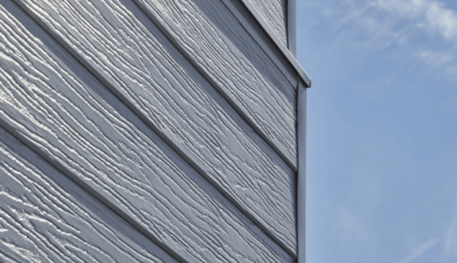 Grijze gevelbekleding met houtnerfstructuur tegen een blauwe lucht.