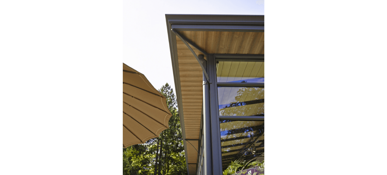 Buitenaanzicht van het gebouw met houten plafond, glazen raam en parasol.