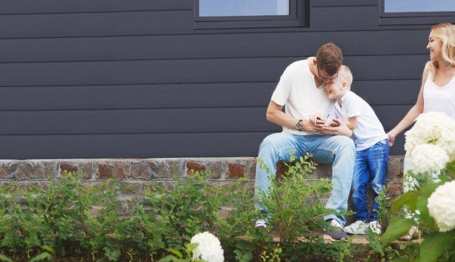 Een gezin van vier zit buiten een huis en kijkt naar een telefoon.