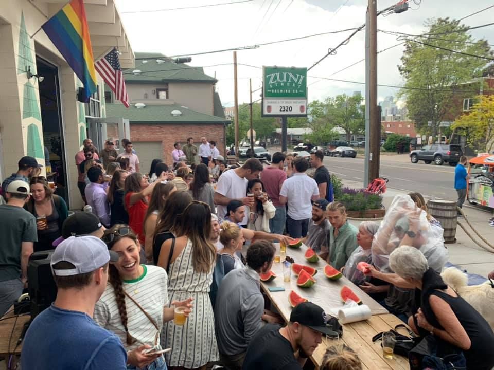 A large group of people are sitting around a table eating watermelon.