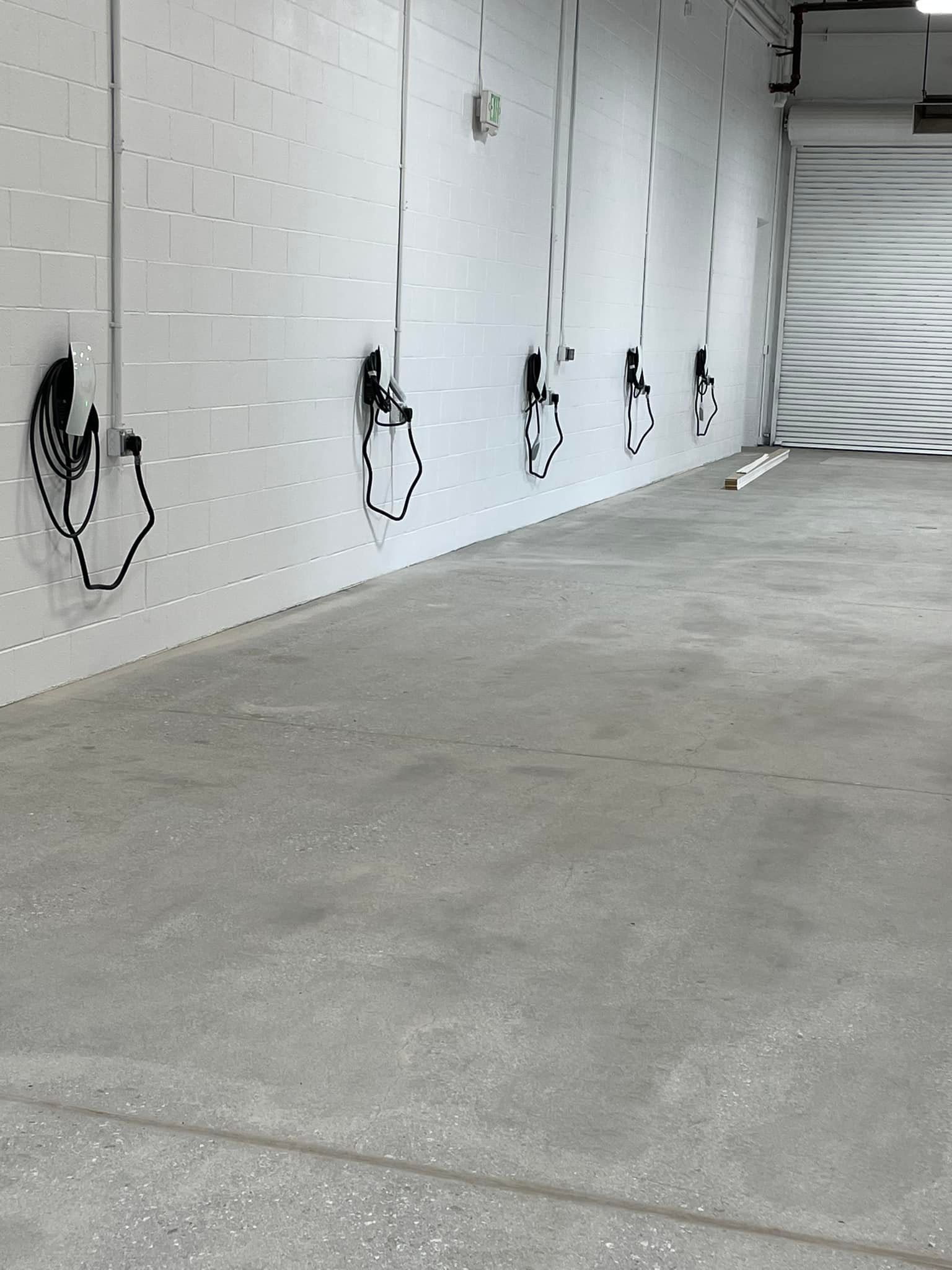 A row of charging stations are lined up against a white wall in a garage.