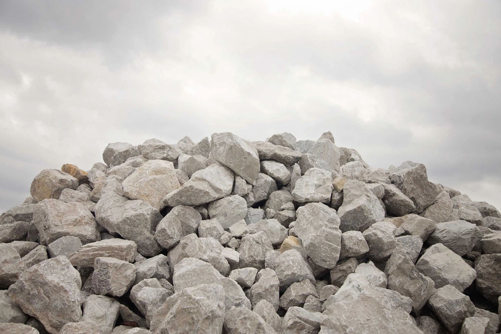 A large pile of gray, jagged crushed stone rocks set against a cloudy, overcast sky.