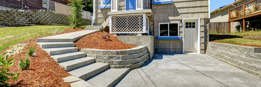 A house with a concrete driveway and stairs leading up to it.