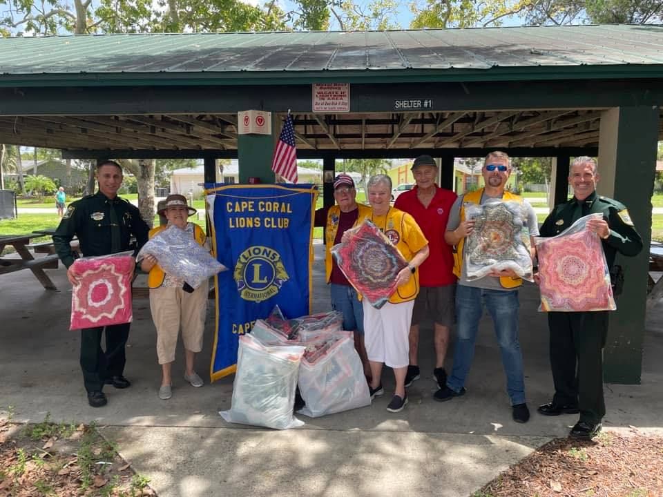 A group of people are standing under a pavilion holding blankets.